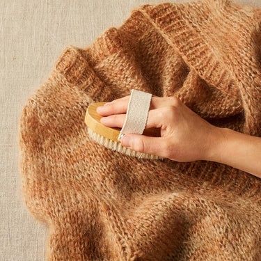 Käsi harjaa ruskeaa villapaitaa vaateharjalla