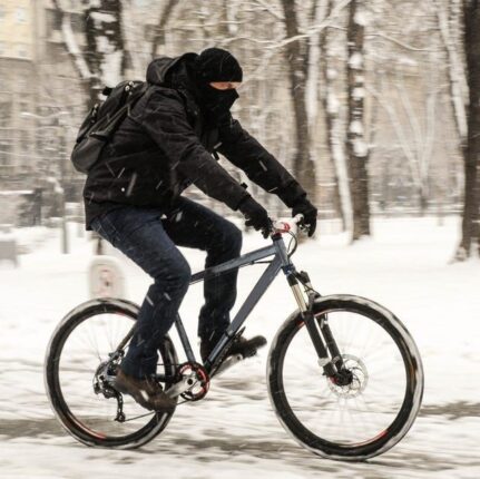 Talvivaatteisiin pukeutunut pyöräilijä ajaa lumisella kadulla