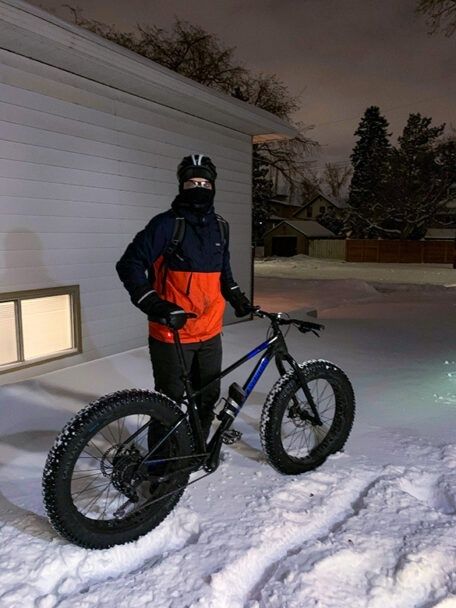 Talvipyöräilijä nastarenkaisen fatbiken kanssa lumisella pihalla